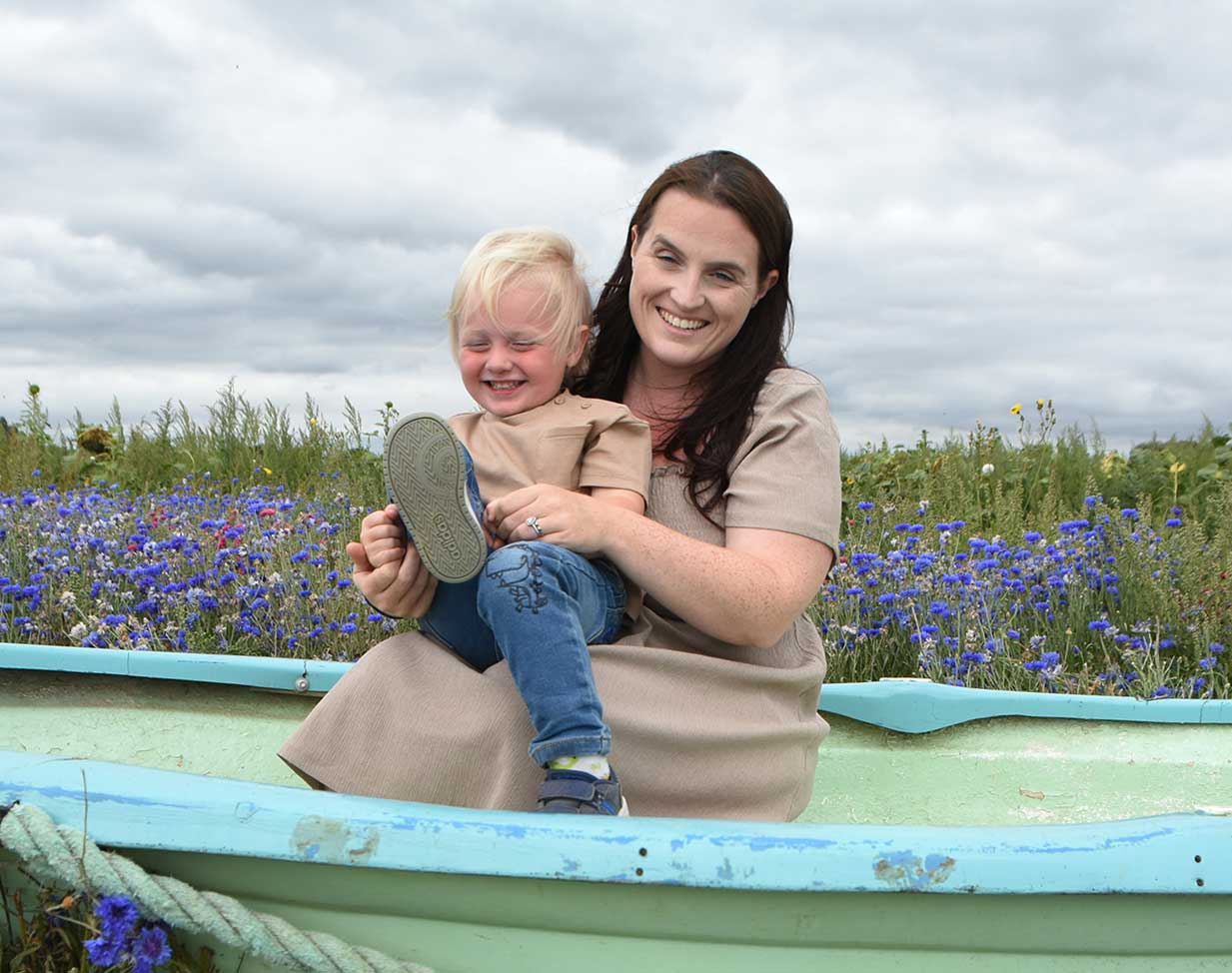 Mother and 3 year old in blue boat and wild flowers behind them