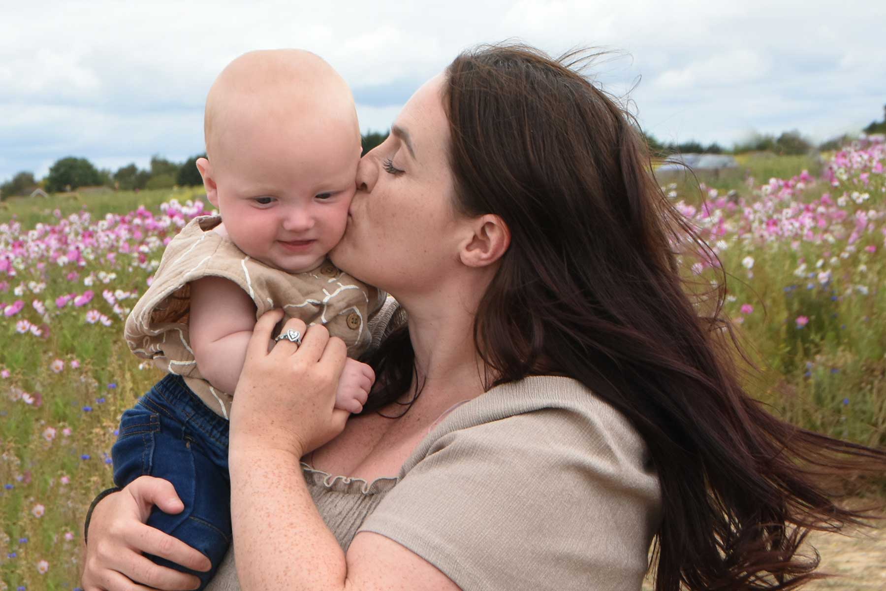 mother and baby. mother kissing baby  wild flowers behind them 
