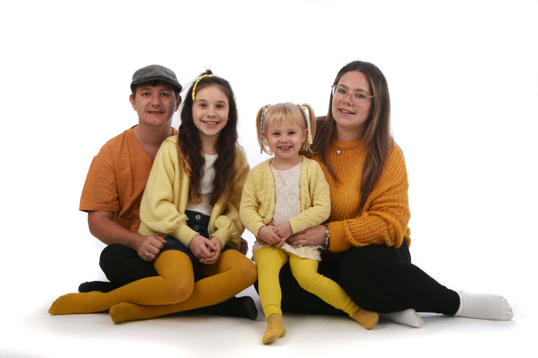 Family of 4 sitting on the ground white backdrop 