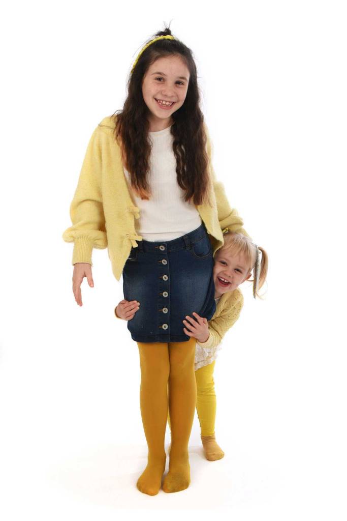 Sisters stood together. Youngest peeping out from behind the other white background